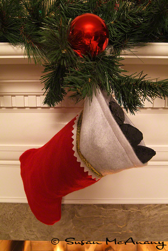 Stocking stuffed with coal with greenery and ornament.